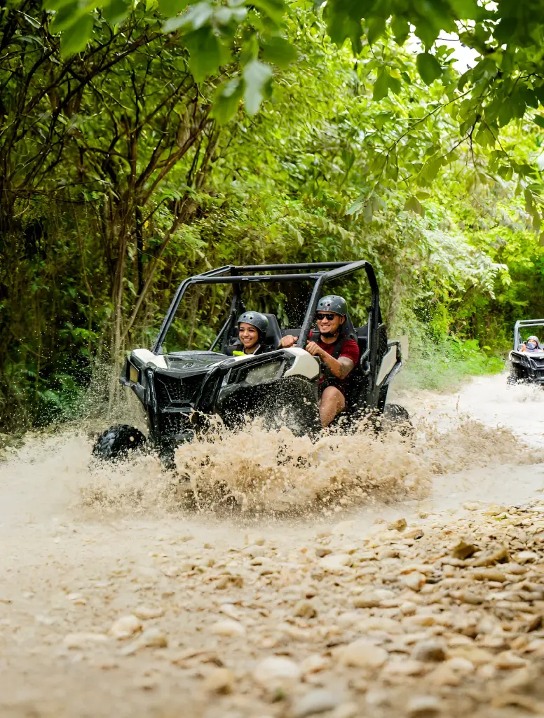 Dos personas con casco conduciendo un buggy que levanta el barro de un camino de montaña