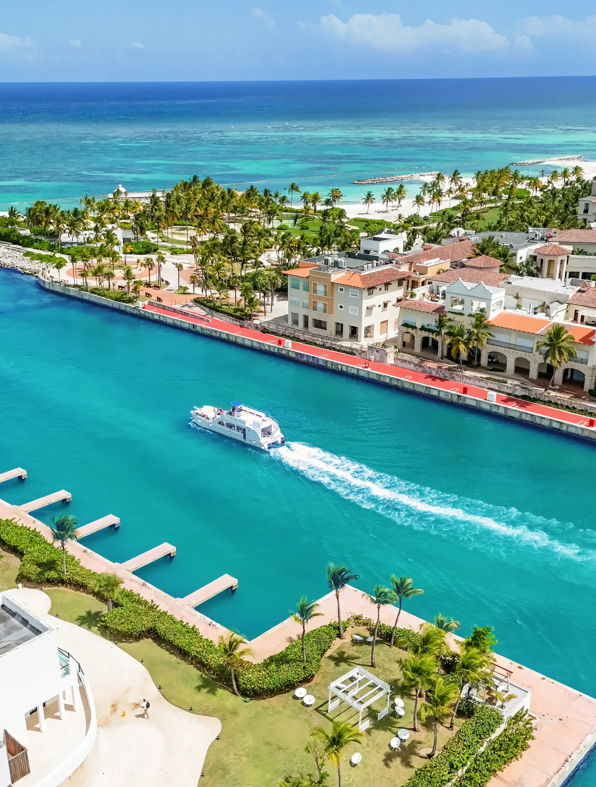 Vista aérea de la marina de Punta Cana: un yate navegando por el canal turquesa entre palmeras y villas
