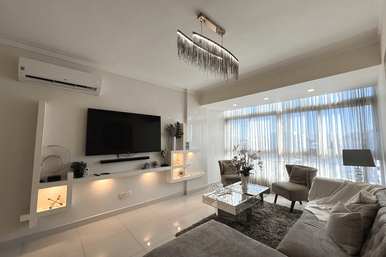 Salón moderno y luminoso de un apartamento de lujo, con gran ventanal, sofá y televisión, en la República Dominicana