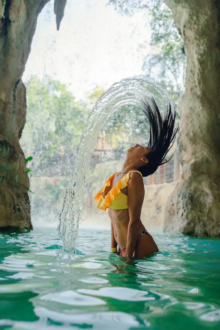 Mujer bañándose bajo la cascada de una cueva de aguas turquesas