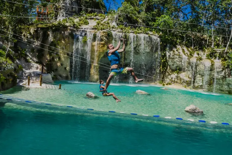 Persona saltando a la piscina turquesa junto a una cascada, en Monkey Jump