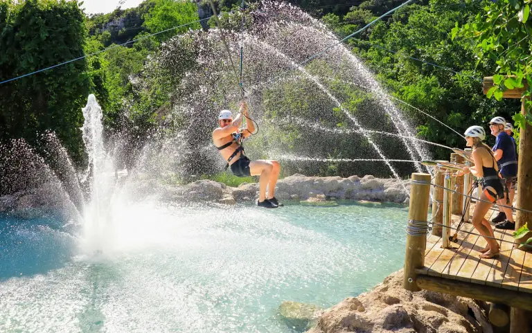 Persona en tirolina atravesando los chorros de agua de una fuente
