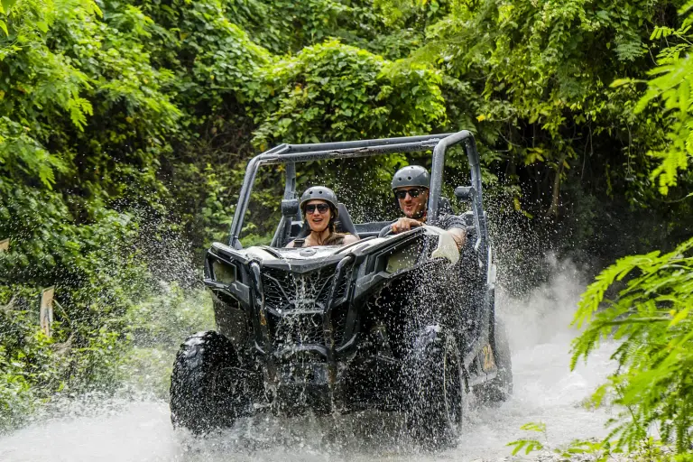 Dos personas conduciendo un buggy que levanta barro en un sendero de la selva