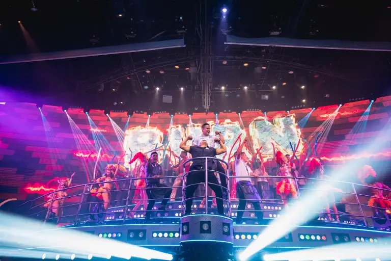 Cuerpo de baile sobre el escenario con luces rosas y moradas