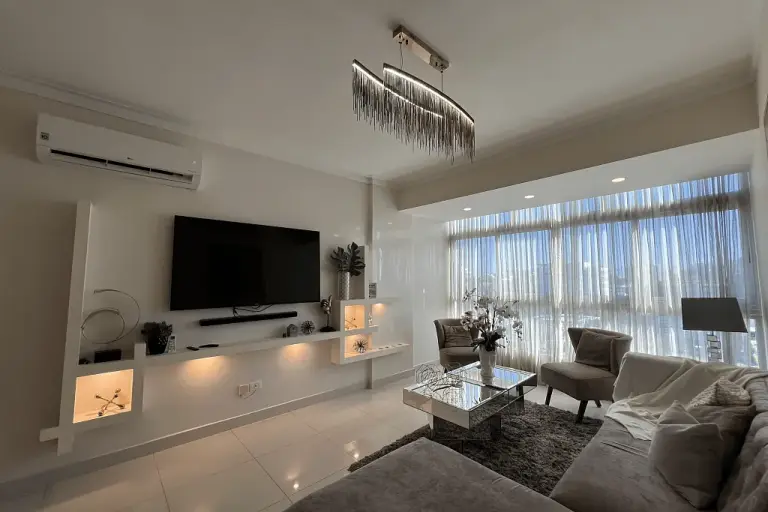 Salón moderno de un apartamento de lujo, con gran ventanal, sofá y televisión, en la República Dominicana